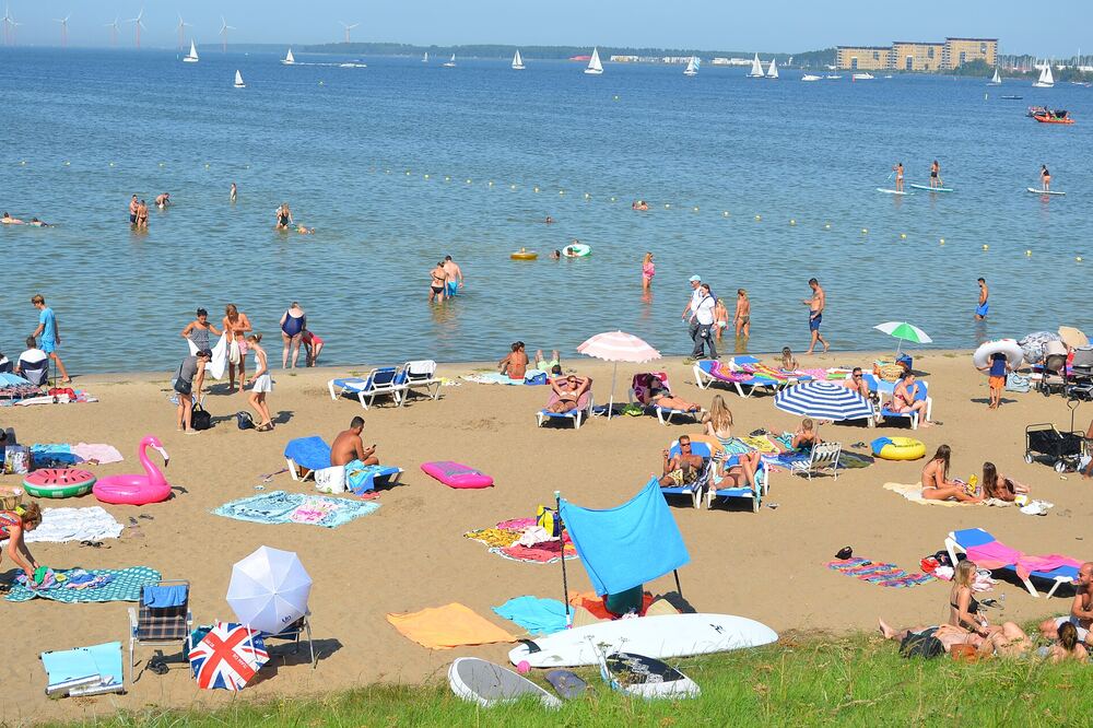 Druk zandstrand aan het Gooimeer met zonnende badgasten, zwemmers en zeilboten op het water